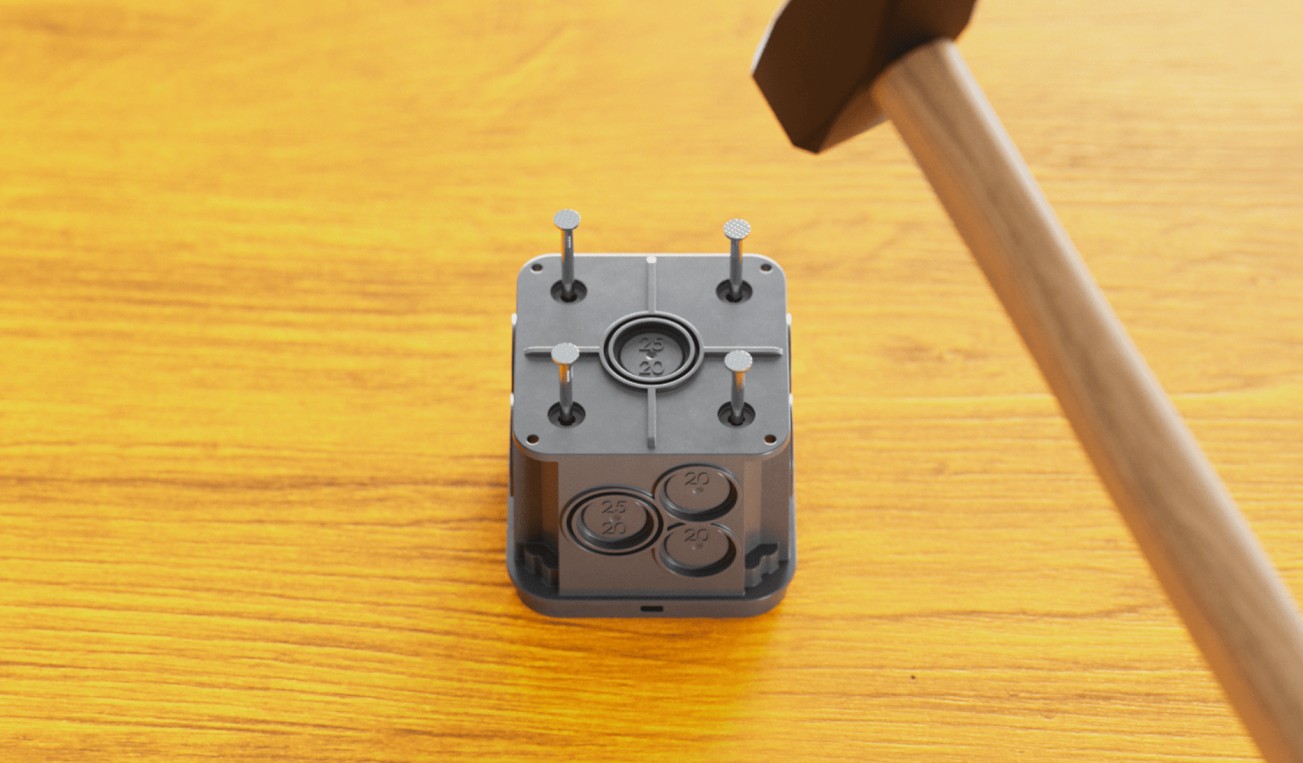 Ein Hammer nähert sich einem grauen Block, in den mehrere Nägel teilweise eingeschlagen sind und der auf einer Holzfläche liegt. Der Block hat runde, beschriftete Abschnitte und vier aufrechte Nägel, die auf der Oberseite sichtbar sind.