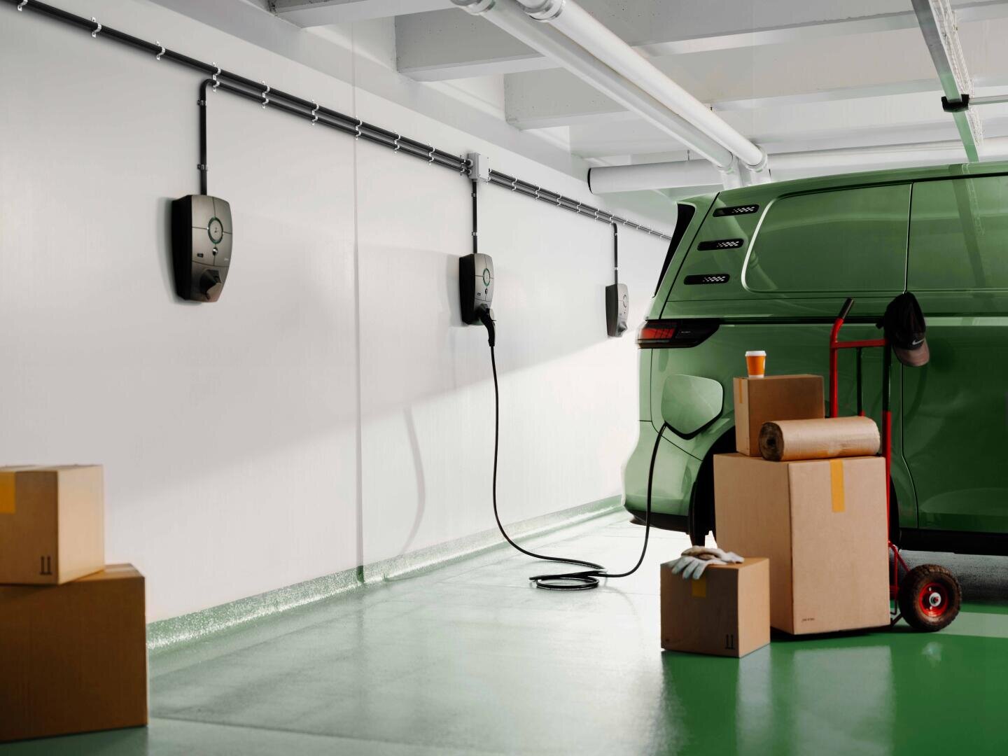 Ein umweltfreundlicher Elektro-SUV wird in einer sauberen Garage aufgeladen. Daneben stehen Kartons, ein aufgerollter Teppich und eine Tasse, was auf einen Umzug oder das Auspacken hindeutet. An der weißen Wand sind mehrere Ladestationen für Elektrofahrzeuge angebracht.