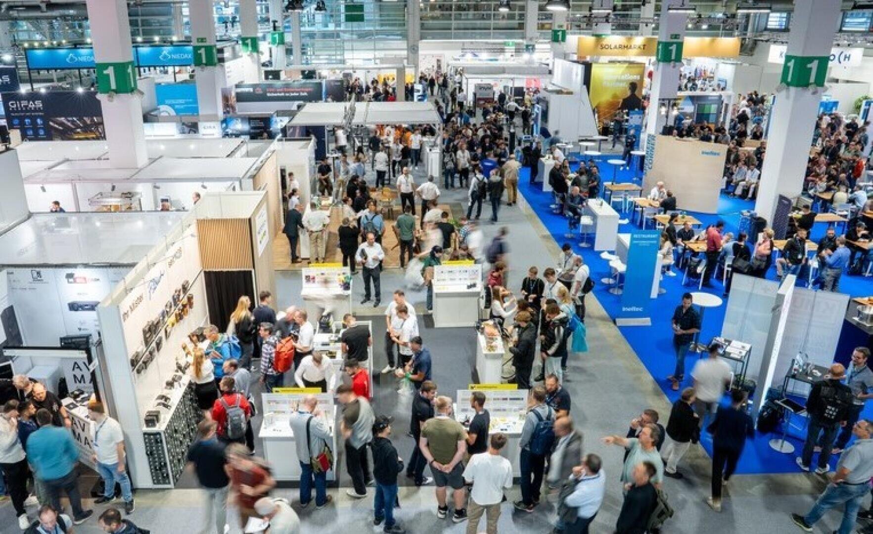 Ein belebtes Kongresszentrum mit vielen Menschen, die zwischen den Ständen und Exponaten umhergehen. Die Teilnehmer interagieren mit den Verkäufern und erkunden die Auslagen bei heller Beleuchtung in einem großen, offenen Raum.
