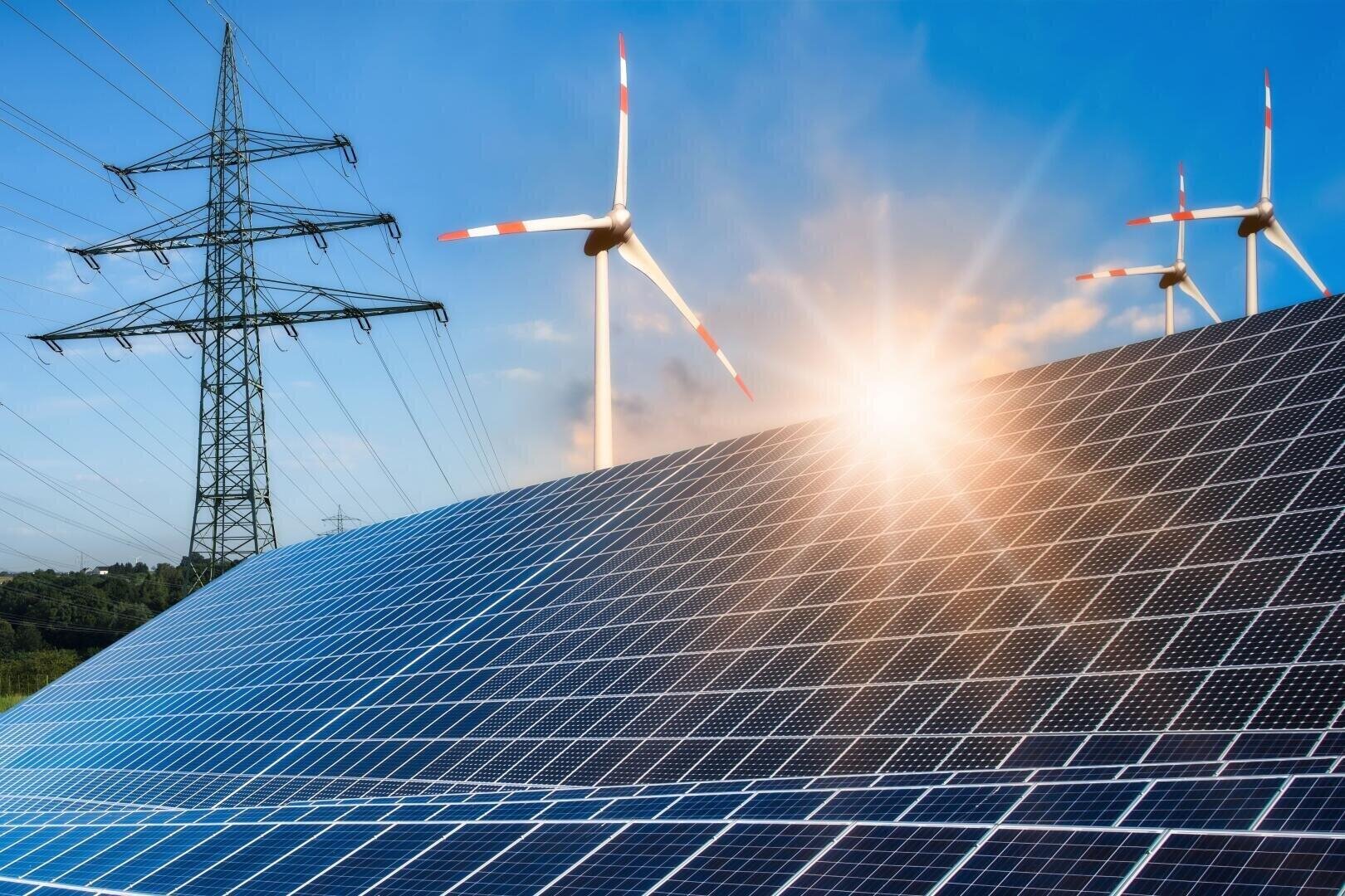 Au premier plan, des panneaux solaires sous un soleil radieux ; à l'arrière-plan, des éoliennes en rotation et un pylône électrique se découpant sur un ciel bleu – un symbole des énergies renouvelables.