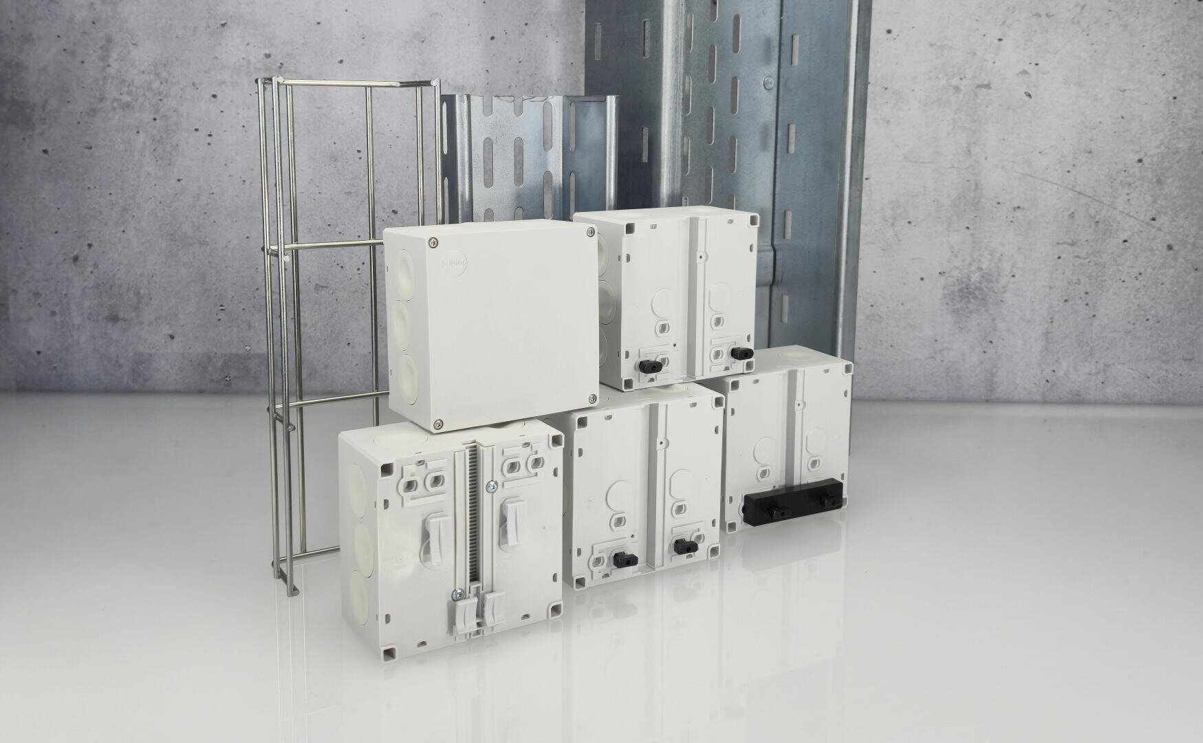 Groupe de boîtes de dérivation électriques blanches et d'accessoires métalliques de gestion des câbles disposés sur une surface réfléchissante, avec un arrière-plan en béton gris de style industriel.
