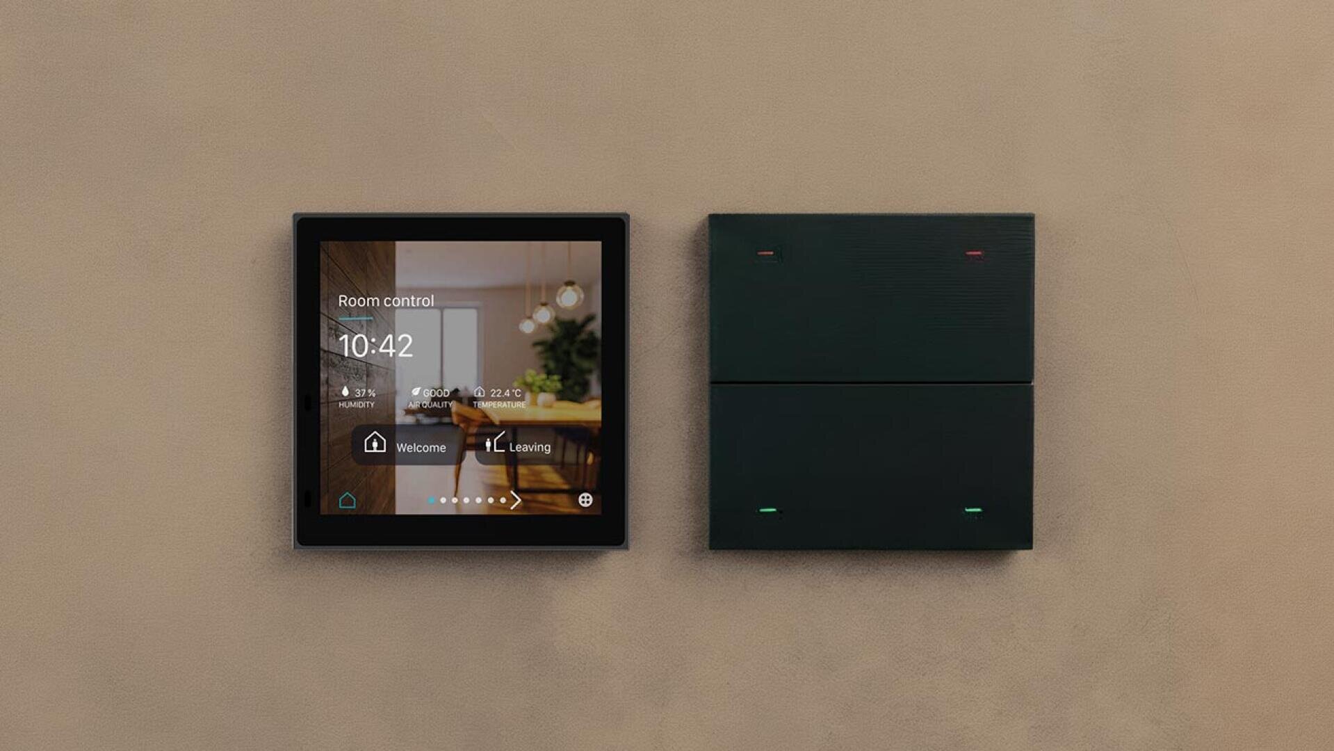 Ein modernes digitales Raumbediengerät zeigt Zeit, Temperatur, Luftfeuchtigkeit und Beleuchtungseinstellungen neben einem dunklen rechteckigen Gerät mit Kontrollleuchten an, die beide an einer beigen Wand angebracht sind.