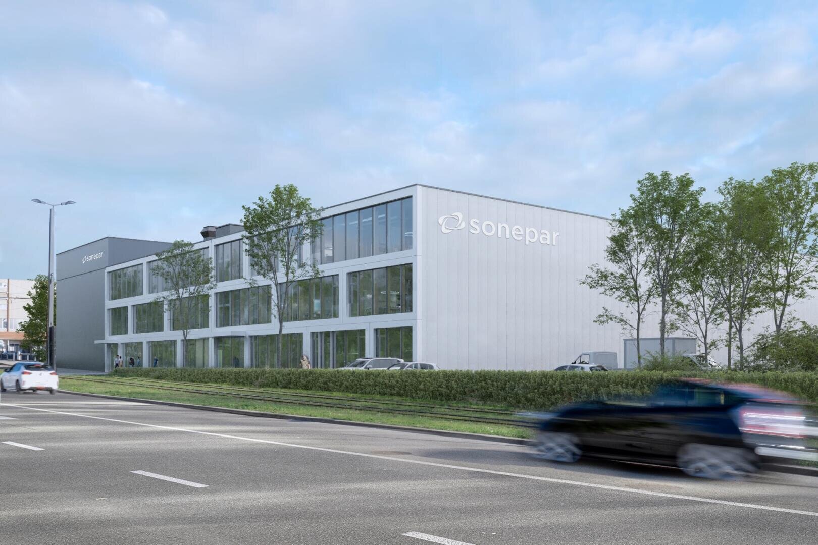Ein modernes, weißes Bürogebäude mit dem Schriftzug „Sonepar“, großen Fensterfronten und umgeben von Bäumen. Draußen stehen Autos, und im Vordergrund fährt ein Auto auf der Straße vorbei, unter einem bewölkten Himmel.