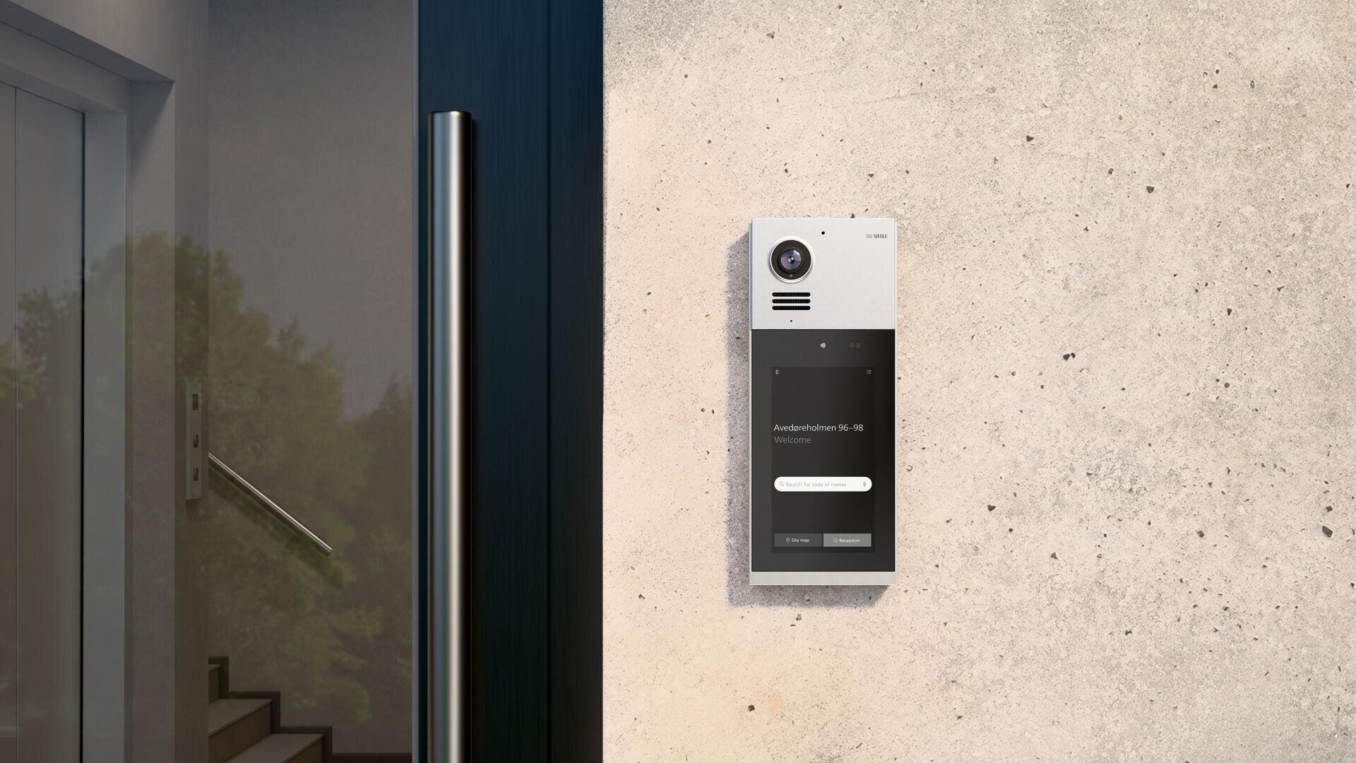 Un interphone vidéo moderne est fixé sur un mur en béton gris clair, à côté d'une porte vitrée ; les arbres se reflètent dans la vitre.