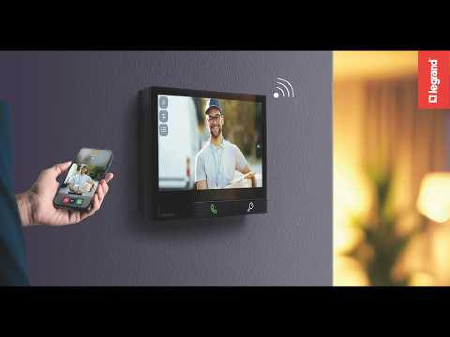 Une personne utilise un smartphone pour interagir avec un système de sonnette vidéo mural affichant un livreur sur son écran. Le système est fabriqué par Legrand.