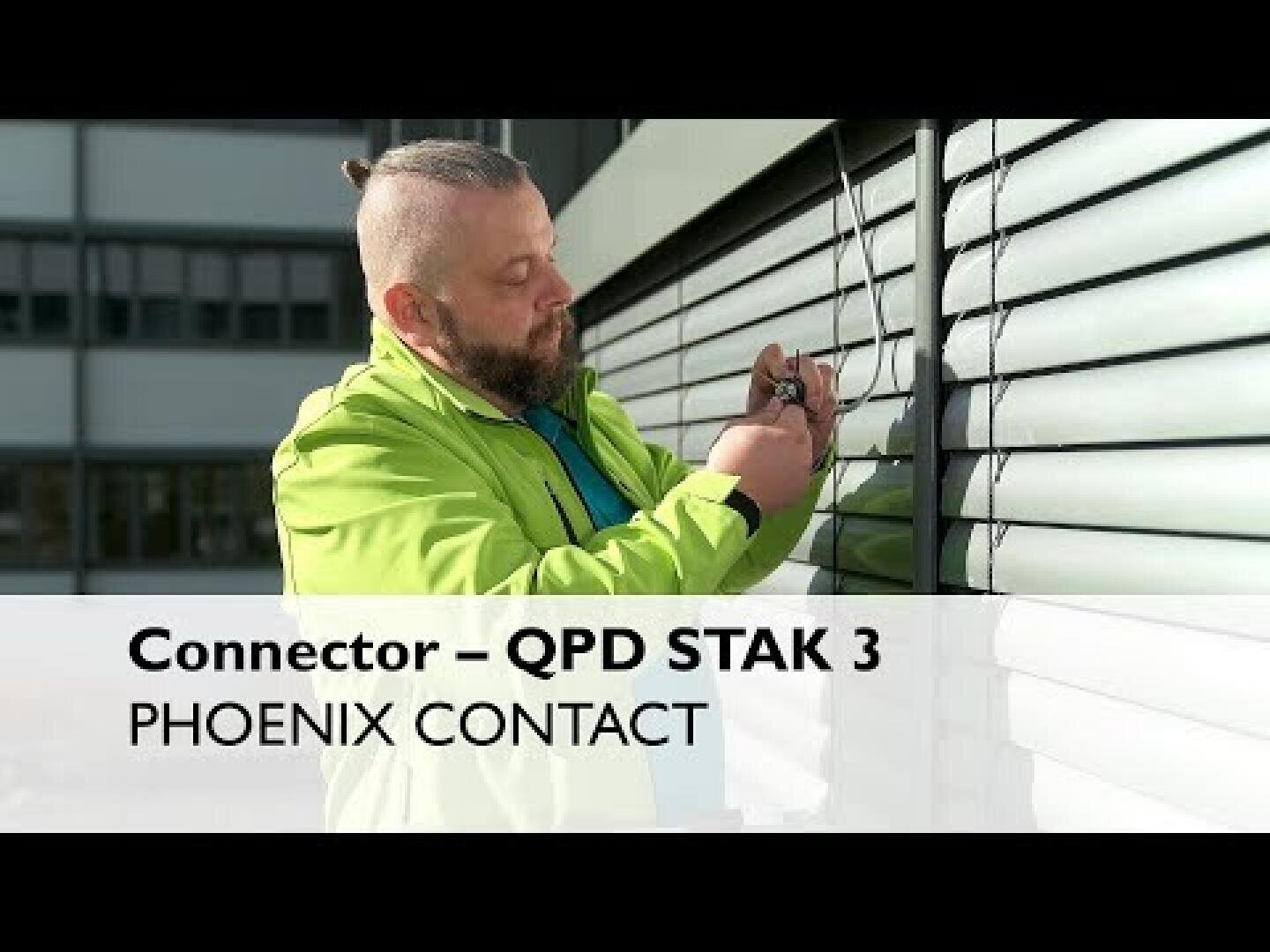 Ein Mann in grüner Jacke installiert Leitungen an einer Außenwand mit horizontalen Metalllamellen. Der überlagerte Text lautet: Anschluss - QPD STAK 3 PHOENIX CONTACT.