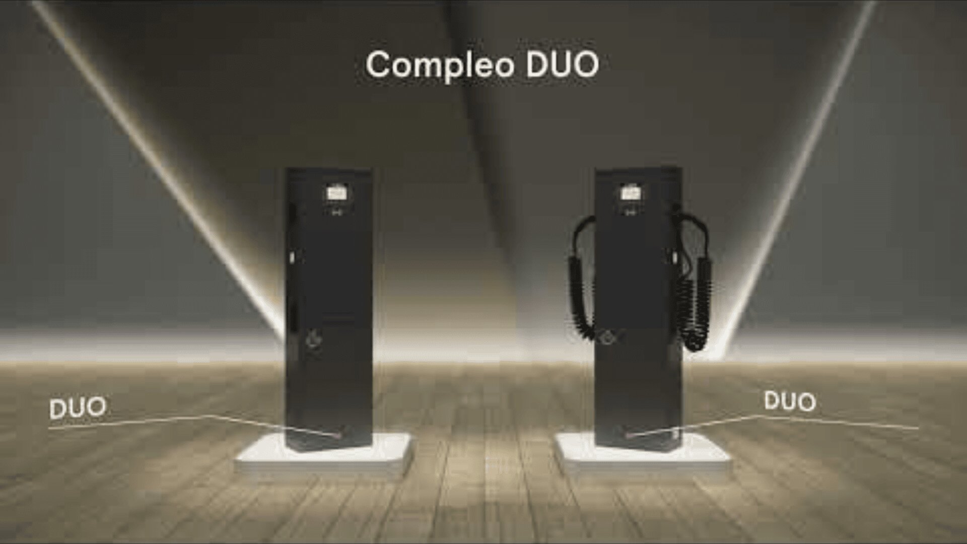 Zwei schwarze Compelo DUO Ladestationen für Elektrofahrzeuge stehen auf einem Holzboden, eine davon mit aufgewickelten Ladekabeln auf der rechten Seite und beide mit der Aufschrift DUO. Der Hintergrund ist dramatisch beleuchtet, darüber steht der Text Compleo DUO.