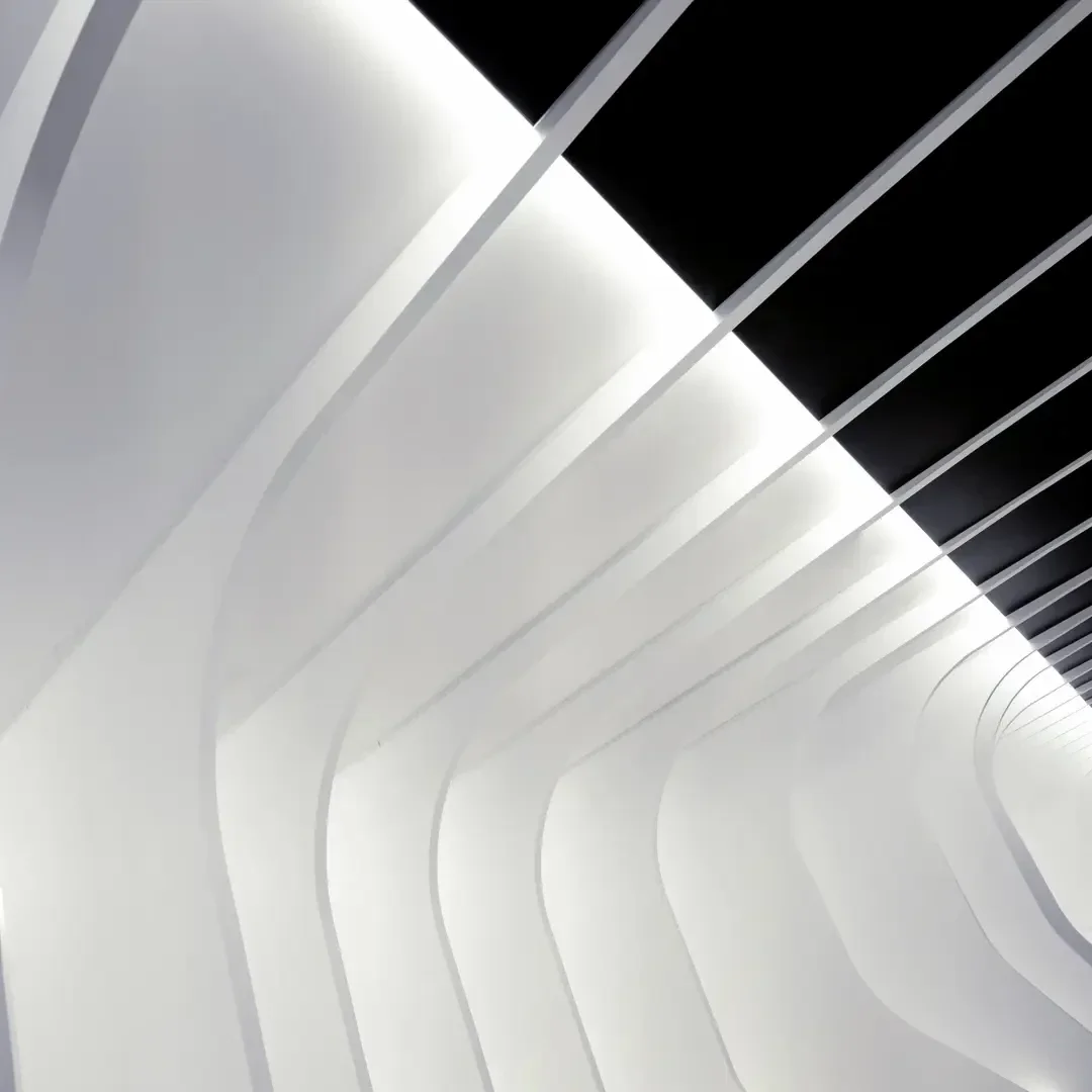 Geschwungene weiße Architekturträger bilden einen tunnelartigen Korridor, der von hellweißen Leuchten beleuchtet wird, während schwarze Paneele an der Decke für Kontrast in einem modernen, minimalistischen Design sorgen.