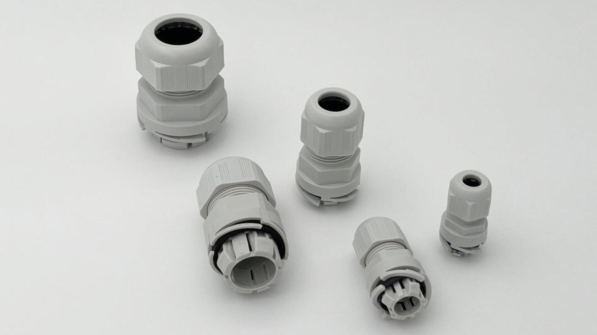Fünf graue Kunststoff-Kabelverschraubungen unterschiedlicher Größe sind auf einem schlichten weißen Hintergrund angeordnet.