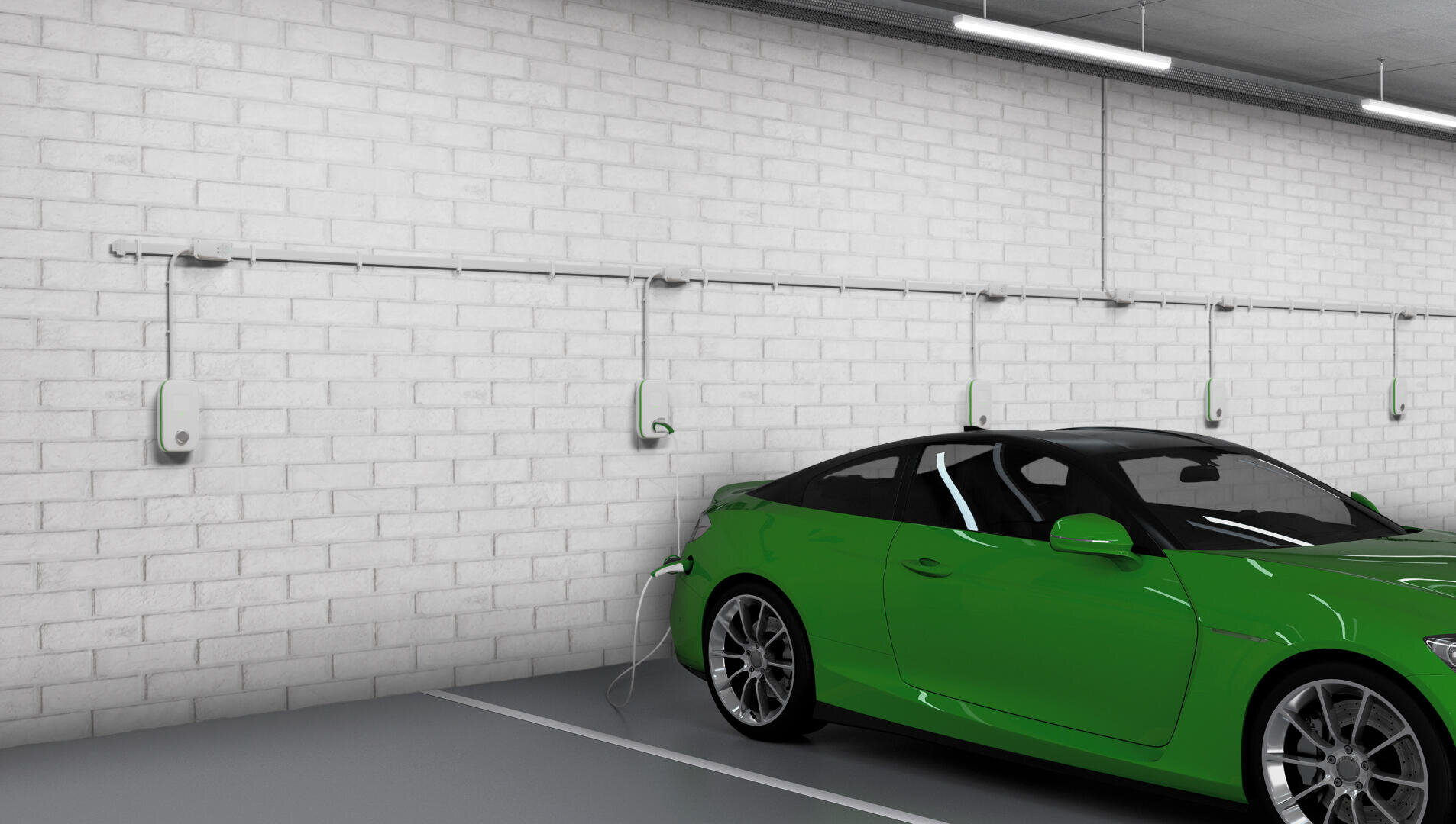 Ein grünes Elektroauto steht in einer Ladestation in einer Halle und ist an eine an der Wand montierte Ladestation angeschlossen, die an einer weißen Ziegelwand angebracht ist. Entlang der Wand sind mehrere weitere Ladestationen zu sehen.