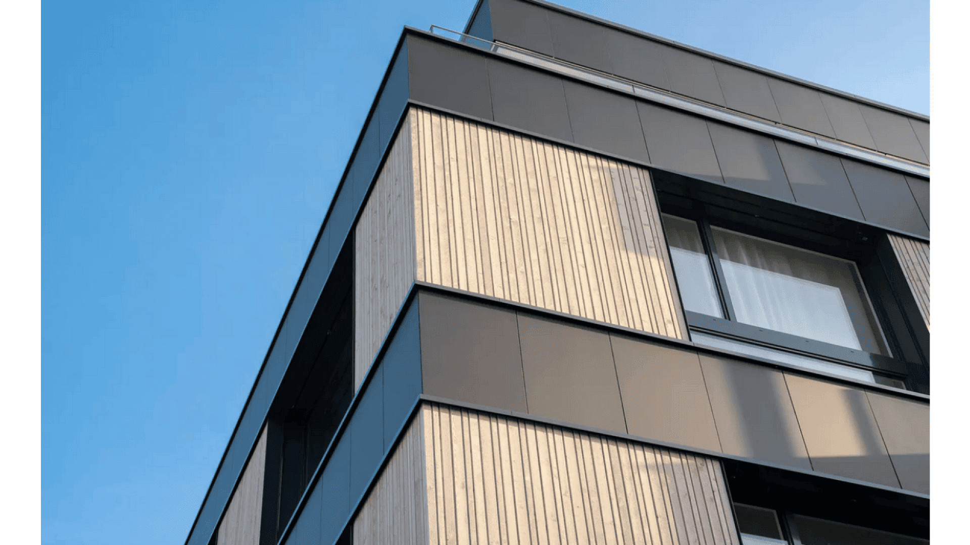 Façade d'un bâtiment moderne avec des lattes de bois verticales et des panneaux métalliques noirs, vue en contre-plongée sur un ciel bleu clair. De grandes fenêtres reflètent le ciel, ajoutant au style architectural contemporain.