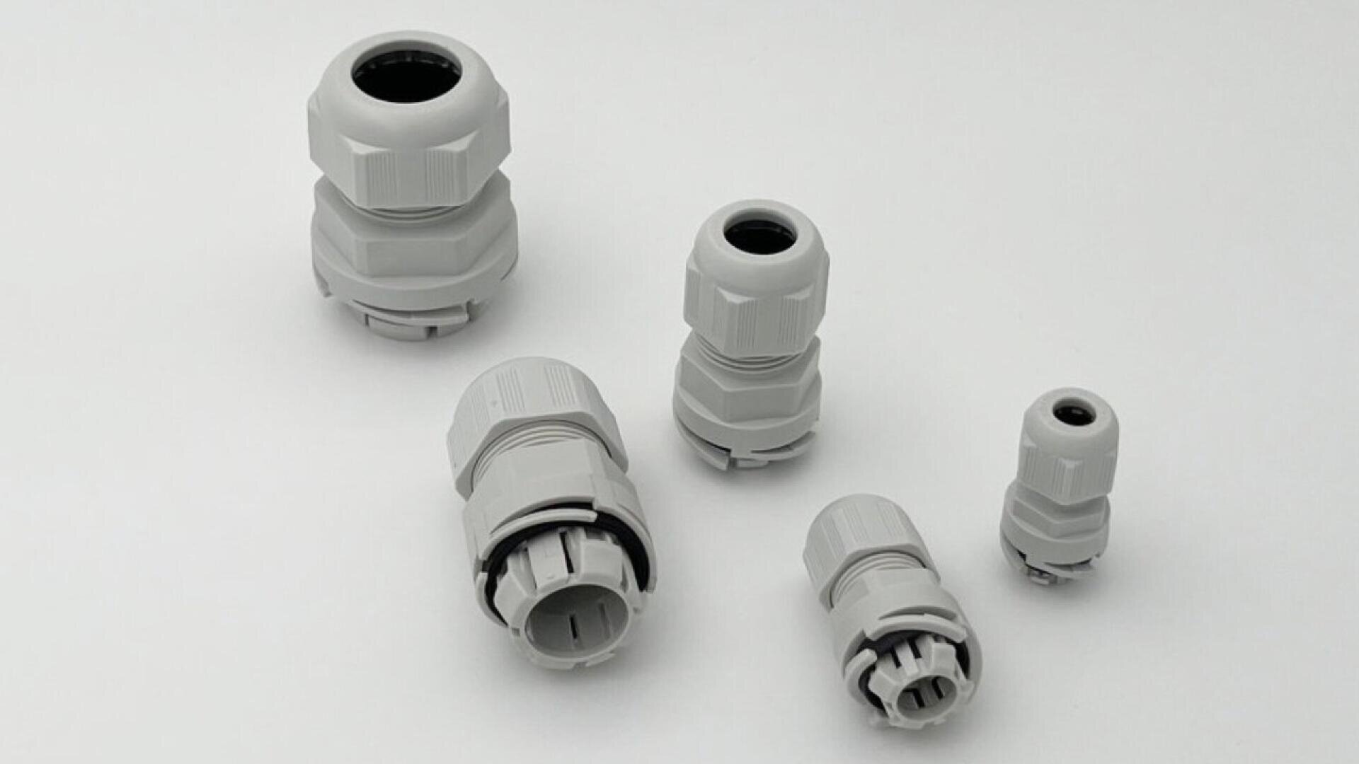 Cinq presse-étoupes en plastique gris de différentes tailles sont disposés sur un fond blanc uni.