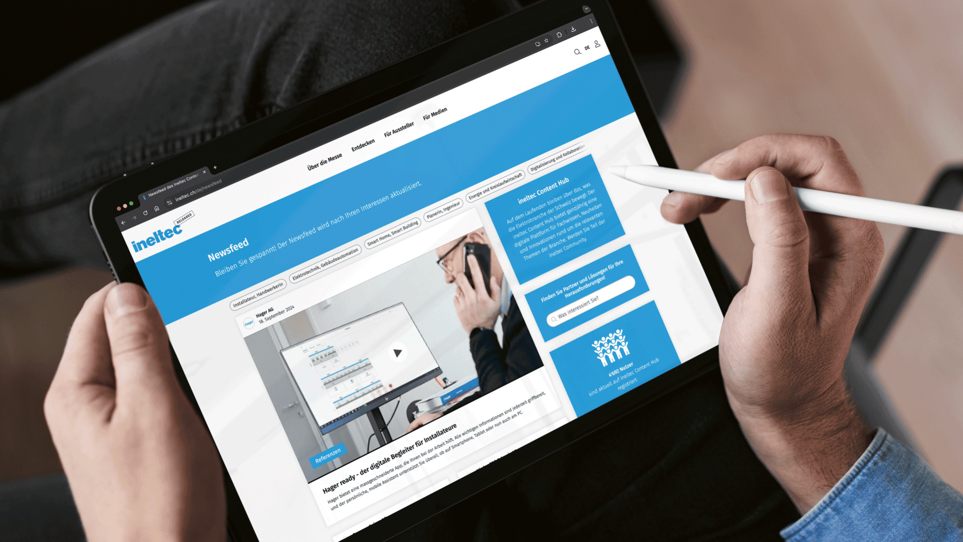 Eine Person verwendet einen Stift, um auf einem Tablet zu navigieren, auf dem die Inteltec-Website mit blauen und weißen Farben, einem Videoplayer, Navigationsregisterkarten und Informationsbereichen angezeigt wird.