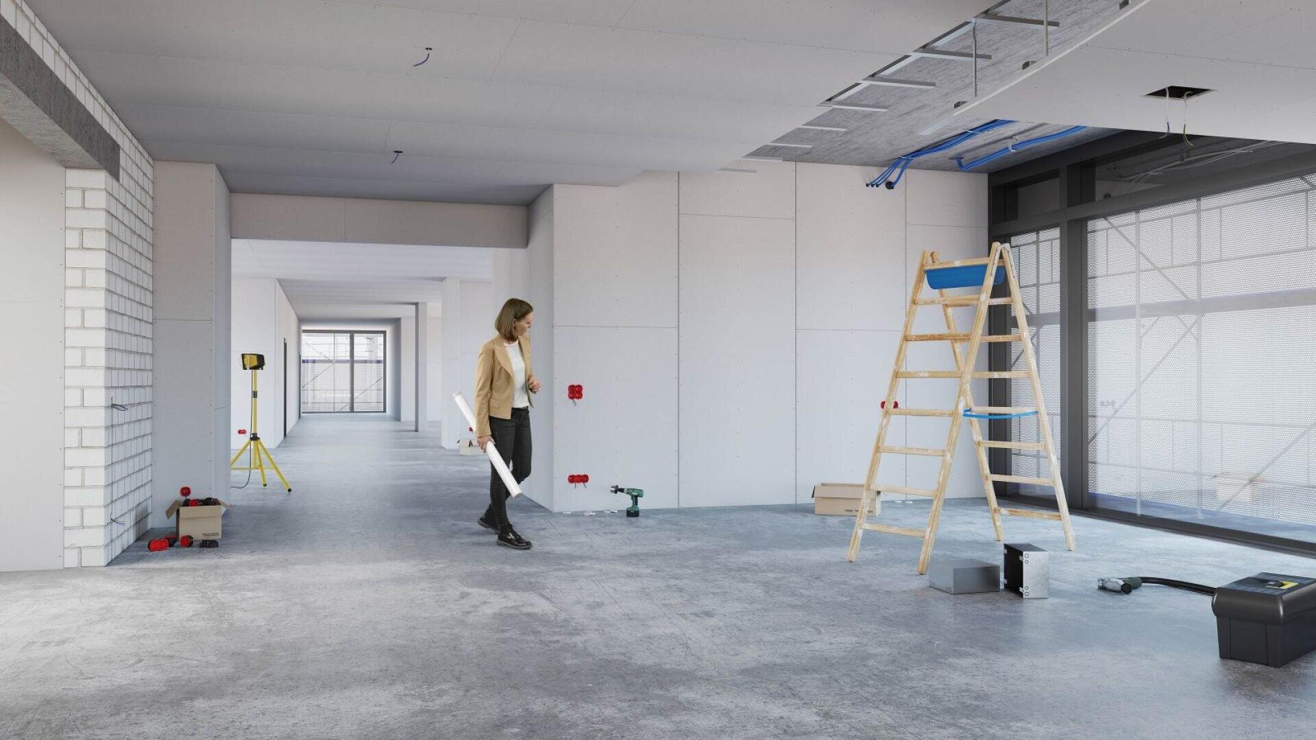 Une femme se promène, plans de construction à la main, dans une grande pièce inachevée où des outils, une échelle et des matériaux de construction sont éparpillés sur le sol en béton.