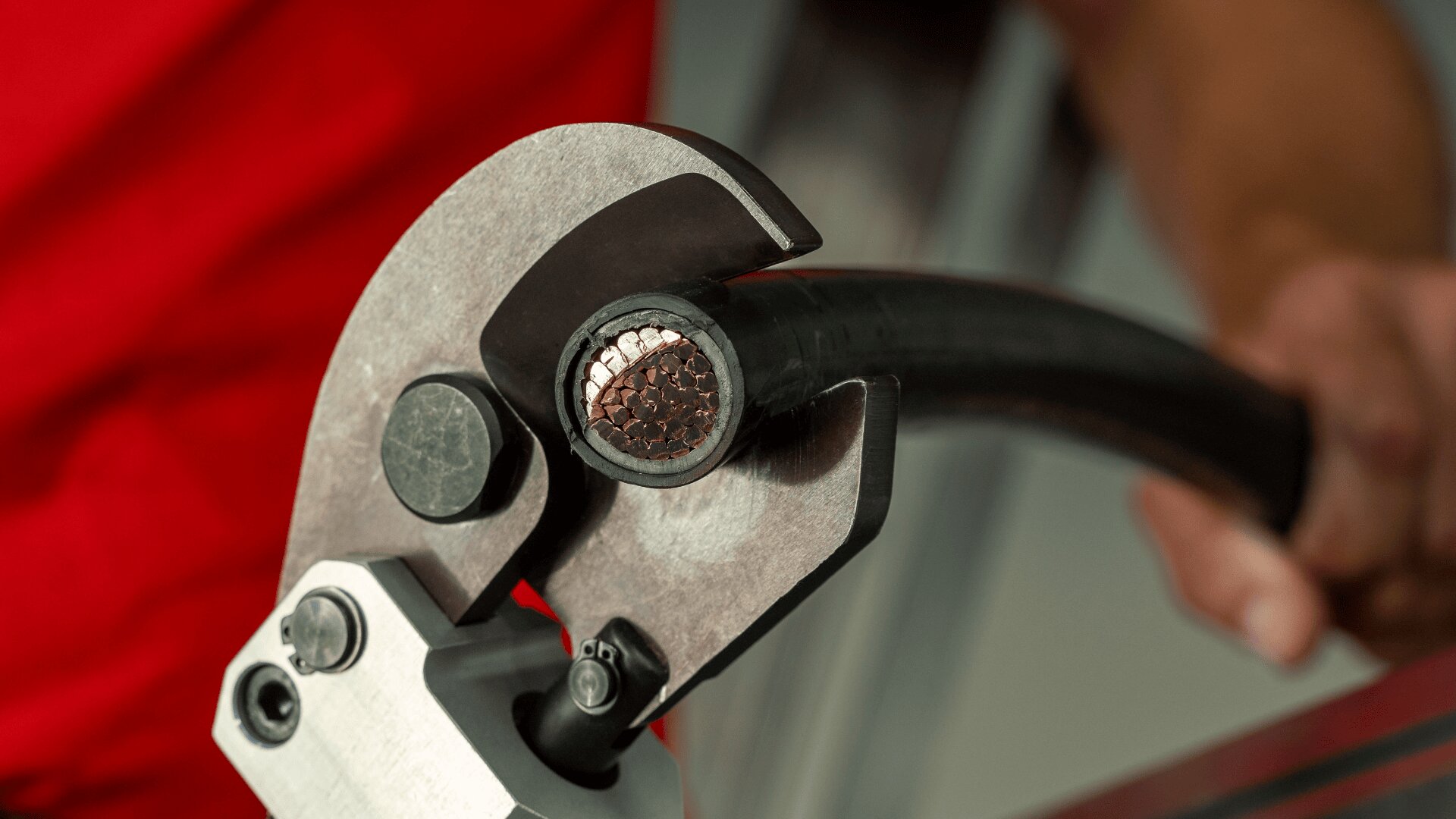 Gros plan d'une personne utilisant un coupe-câble métallique pour couper un câble électrique noir et épais, exposant les fils de cuivre à l'intérieur.