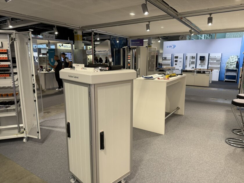 Ausstellungshalle mit Vitrinen, Schalttafeln und Ständen. Im Hintergrund stehen Menschen und unterhalten sich. Der Bereich ist gut beleuchtet und mit Teppichboden ausgelegt; dort sind verschiedene technische Geräte ausgestellt.