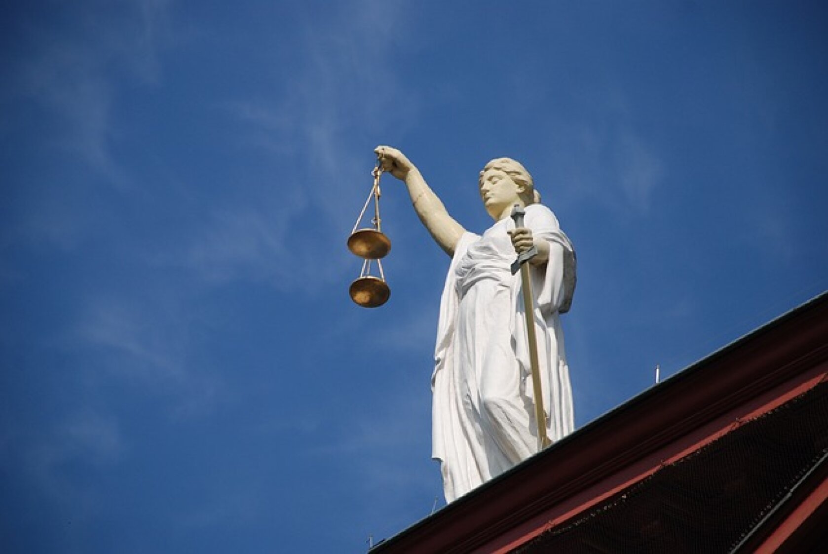 Sous un ciel d'un bleu éclatant, une statue de la Justice, tenant une balance et une épée dans ses mains, se dresse sur le toit d'un immeuble.