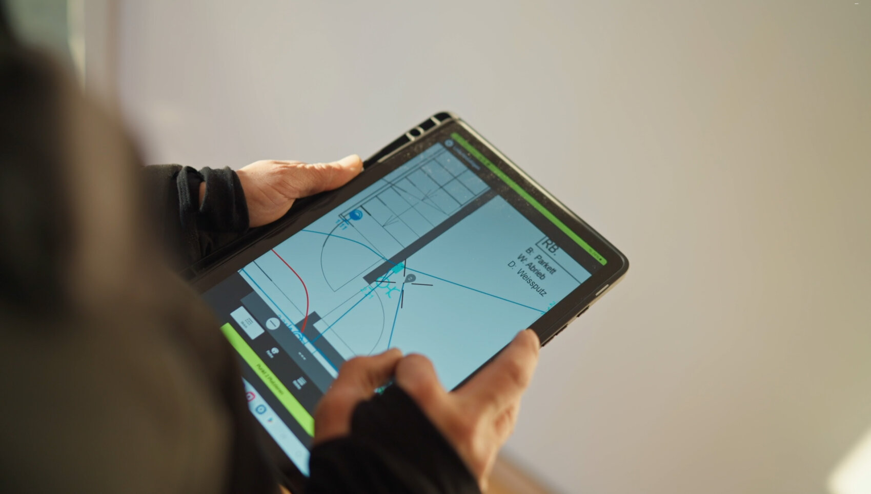 Eine Person hält ein Tablet in der Hand, auf dem eine Navigations- oder Kartenanwendung angezeigt wird, die eine Route und eine Wegbeschreibung auf einer digitalen Karte anzeigt.